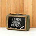 Nahaufnahme der grünen Kosmetiktasche mit Tafeldruck, Reißverschluss und braunem Griff. - Stil 5 (LEARN GROW REPEAT)