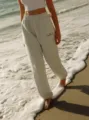 Detailed shot of casual heather grey joggers with blue embroidery, styled on beach background. - XS / Bottoms / Light Gray