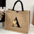 Detail shot of a large burlap tote bag featuring a floral letter A print and black handles. - Floral Alphabet-A