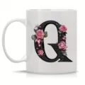 Detailed view of white ceramic coffee mug featuring ornate black letter Q with pink roses design. - Letter Q