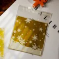 Close-up of clear self-adhesive cellophane candy gift bag with delicate gold snowflake pattern. - 100 Pieces/Pack (10*10+3cm) / Gold Background Snowflake