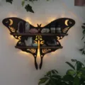 Detailed shot of a wooden Luna moth crystal wall shelf with warm LED backlighting and stones. - Moth