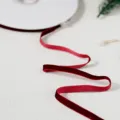 Detail close-up of a dark red velvet ribbon unwinding on texture background for gift wrapping. - Burgundy