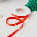 Detailed shot of red Christmas ribbon featuring gold foil printed merry christmas text and bell icon. - Red