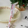 Christmas ribbon detail shot, white fabric with red holiday text and smiley faces for decor. - White