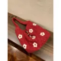 Primo piano di una borsa tote rossa pelosa con ricamo floreale bianco su un tavolo di legno. - Rosso