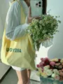 Dettaglio di una borsa a tracolla in tela gialla con stampa di lettere, stile quotidiano. - Giallo