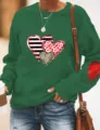 Detailaufnahme des grünen Sweatshirts mit Herzen-Print, Rundhalsausschnitt und Ellenbogen. - Grün