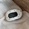 Vue détaillée d'une pince à cheveux en tissu blanc à pois noirs sur fond textile beige. - Pince à Cheveux Pois Blanche