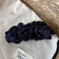 Close-up view of elegant navy blue polka dot hair clip featuring ruffled fabric and clasp. - Pleated Banana Clip / Navy White Polka Dot
