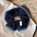 Close-up detail donkerblauwe polkadot haarscrunchie met denim rand en strik label. - Blauwe Rand Geplooide Scrunchie / Marine Wit Gestippeld