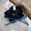 Close-up of dark blue polka dot hair scrunchie detail featuring a denim bow and tag. - Denim Bow Scrunchie / Navy White Polka Dot