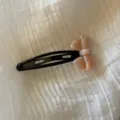 Detalle en primer plano de un bonito pasador de pelo con lazo de acetato rosa sobre tela blanca. - Rosa loto