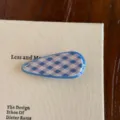 Gros plan d'une pince à cheveux à carreaux bleus et blancs sur une surface de livre texturée. - Pinces à cheveux bec de canard / Bleu
