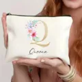 Detalle en primer plano de bolsa de cosméticos blanca con letra floral Q y nombre. - Estilo Q
