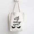 White canvas tote bag with chic makeup quote print and eyelash graphic, casual shoulder bag. - Eat Sleep Makeup Repeat Slogan Style / 35x40cm