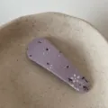 Close-up detail of a cute purple floral fabric snap hair clip resting on a ceramic dish. - Purple Water Drop