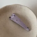 Close-up detail of a purple floral fabric hair clip placed on a minimalist ceramic dish. - Purple Triangle