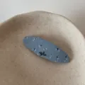 Close-up detail of a blue floral fabric hair clip resting in a minimalist ceramic dish. - Blue Oval