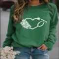 Nahaufnahme Detail des grünen Rundhals-Sweatshirts mit weißem floralen Herz-Stethoskop-Druck. - Grün