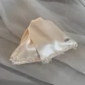 Detailed shot of a champagne satin hair clip with delicate beaded edge and metal handmade tag. - Off White