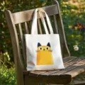 Canvas tote bag detail showing cute yellow cat print on wooden bench in outdoor garden setting. - Yellow Cat Style