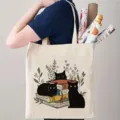 Canvas tote bag featuring a cute black cat and books illustration in a daily commuting scene. - Black Cat Illustration Style