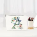 Detailed view of white canvas cosmetic pouch with floral letter A design and makeup brushes. - Letter A