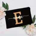Custom black canvas makeup bag with gold letter E and white name print, floral backdrop. - Letter E