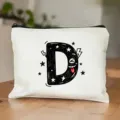 Vue détaillée d'une trousse de maquillage blanche en toile avec un joli imprimé lettre D. - Style Lettre D