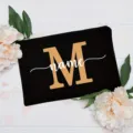 Close-up detail of custom black canvas pouch featuring gold letter M and white name print. - Letter M