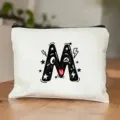 Gedetailleerd overzicht van het witte canvas make-up tasje met een schattig cartoon letter M design. - Letter M
