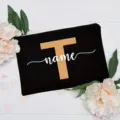 Detailed close-up of a personalized black canvas cosmetic pouch featuring a custom letter and text design. - Letter T