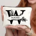Gedetailleerd overzicht van witte canvas make-uptas met zwarte letterprint en elegant bladmotief. - Letter W