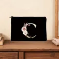 Detail view of a black cosmetic pouch featuring a floral letter C print on a wooden desk. - Letter C