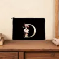 Close up view of black clutch bag featuring a golden floral letter D design on wooden table. - Letter D