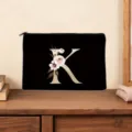 Black cosmetic bag featuring gold letter K and floral print, stylish zipped pouch for daily use. - Letter K
