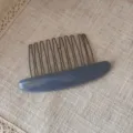 Detailed view of grey-blue acetate hair comb with metal teeth on textured fabric. - Blue