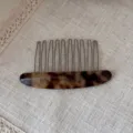 Close-up detail of tortoiseshell acetate hair comb with metal teeth on textured fabric background. - Tortoise