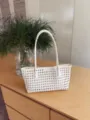 Vista di dettaglio di una borsa tote intrecciata bianca traforata su tavolo di legno. - Bianco