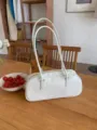 Close-up of a trendy white cylindrical shoulder bag on a wooden table, minimalist design detail. - White