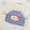 Primo piano del mini grembiule per bambole a quadretti blu e bianchi con ricamo e bottone. - Grembiule a Quadri Perle