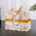 Witte papieren geschenkzak met gouden bloemenmotief, elegante lintstrik en stevige koordhandgrepen. - Gouden Bloemen Effen Gouden Lint / Klein Horizontaal L18 H16 B10cm