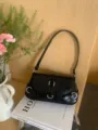 Detailed shot of a black glossy moto style shoulder underarm bag featuring metal buckle accents. - Black