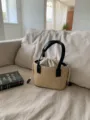 Detailed view of a woven straw bucket bag with black handles and a drawstring closure on a sofa. - Black