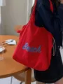 Detail view of the stylish red canvas shoulder bag with letter print and drawstring design. - Red