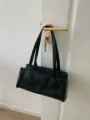Detail view of black vintage baguette shoulder bag hanging on handle, minimalist style. - Black