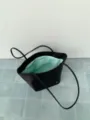 Dettaglio ravvicinato di una borsa shopper in nylon nero con fodera verde menta e manici lunghi. - Nero