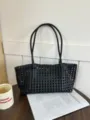 Primo piano di una borsa shopper nera intrecciata con design traforato, chic e capiente. - Nero