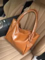 Dettaglio borsa tote in pelle morbida lucida marrone con ciondolo a cuore e catena. - Marrone